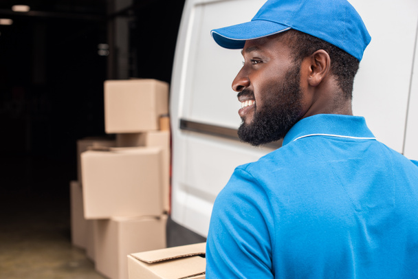 side view of smiling african american delivery man looking away - Fotó, kép