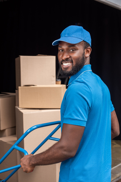 smiling african american courier with cart looking at camera - Foto, immagini