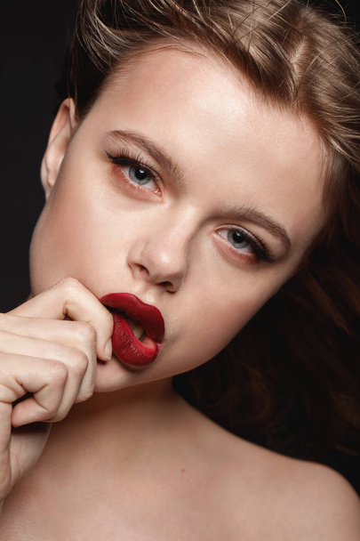 studio fashion portrait of young brunette girl with dark make up touching her red lips on black background. - Φωτογραφία, εικόνα