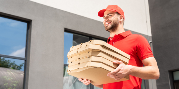 low angle view of smiling caucasian courier carrying pizza boxes - Zdjęcie, obraz