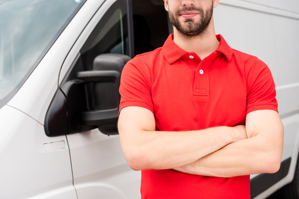 cropped shot of delivery man in red uniform with arms crossed standing at van - Foto, immagini