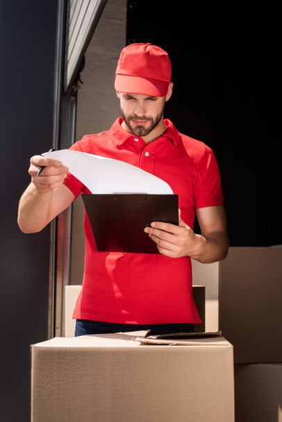 portrait of delivery man in uniform checking notes in notepad - Фото, изображение