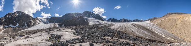 Amazing panorama of a beautiful glacier with cracks, snow, stones and ice breaks high in the mountains against a blue sky with clouds - Photo, image