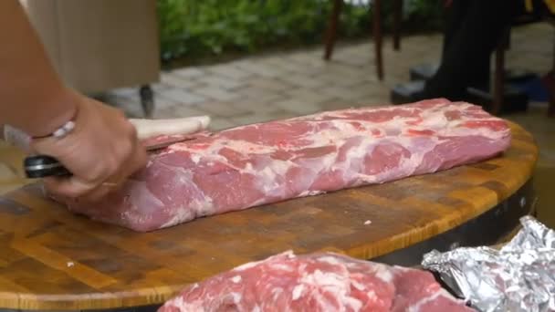 Cook in white gloves cuts off pieces of steaks from a large piece of raw meat. Quality pork tenderloin for the preparation of delicious dishes. Sharp knife and a wooden board. Meat processing before - Footage, Video