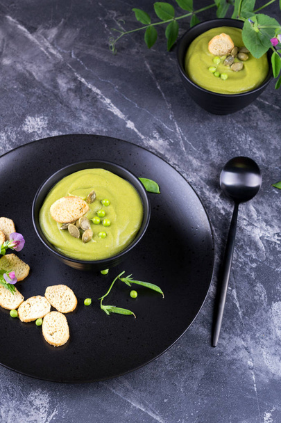 Легкий літній смачний зелений гороховий вершковий суп, поданий з гарбузовим насінням, грінками на темному фоні. плоский лежак
. - Фото, зображення