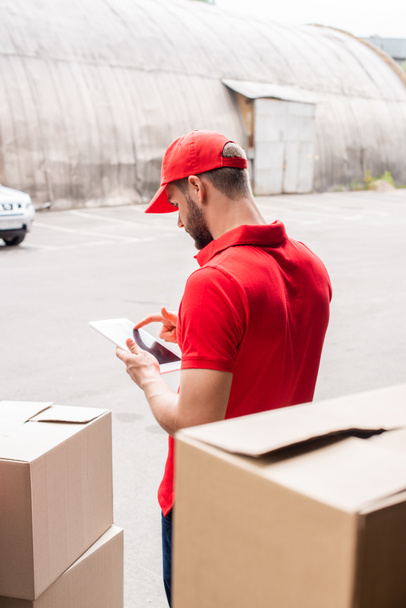 side view of delivery man in red uniform using digital tablet - Foto, Imagem