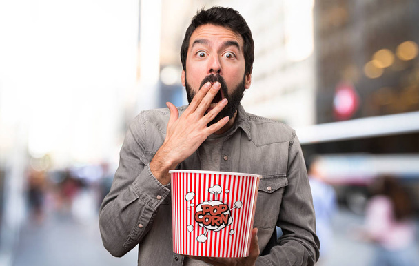Sorprendido Hombre guapo con barba comiendo palomitas al aire libre
 - Foto, imagen