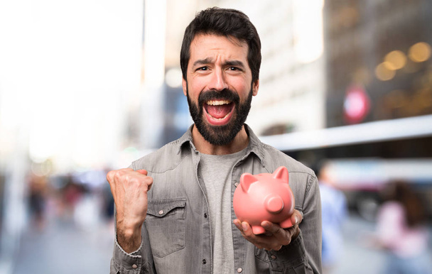 Handsome man with beard holding a piggybank at outdoor - 写真・画像