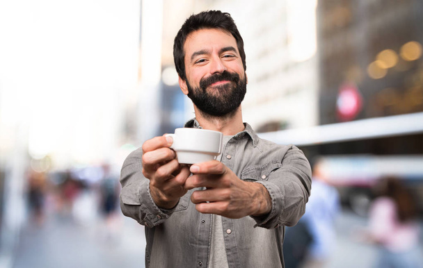 schöner Mann mit Bart, der draußen eine Tasse Kaffee hält - Foto, Bild