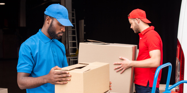 vista laterale di uomini di consegna multietnici in uniforme rossa e blu con scatole di cartone
  - Foto, immagini