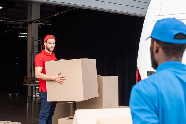 multicultural delivery men in red and blue uniform with cardboard boxes  - Foto, imagen