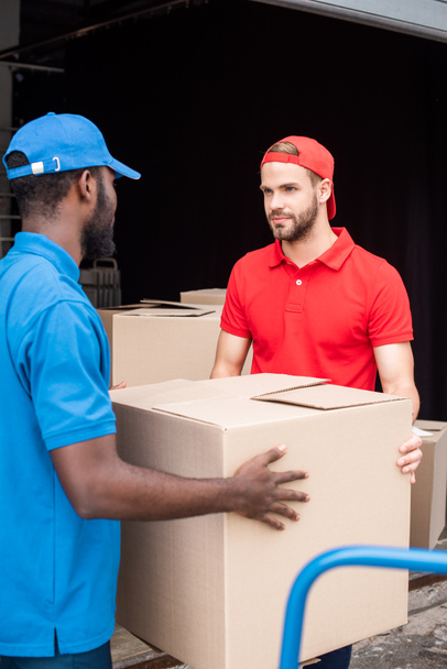 multicultural delivery men in red and blue uniform with cardboard boxes  - Photo, Image