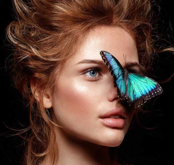 close up portrait of beautiful blonde woman with red lips and blue exotic butterfly sitting on her face - Zdjęcie, obraz