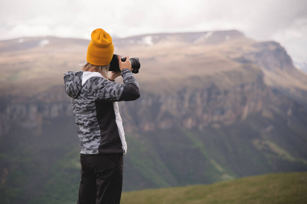 A young girl takes pictures of a plateau on top of a high mountain on a cloudy day. View of the girl behind - Photo, image