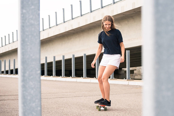 Young Beautiful Blonde Girl Riding Bright Skateboard on the Bridge - Φωτογραφία, εικόνα