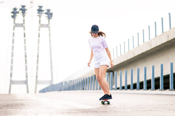 Young Beautiful Blonde Girl Riding Bright Skateboard on the Bridge - Photo, image