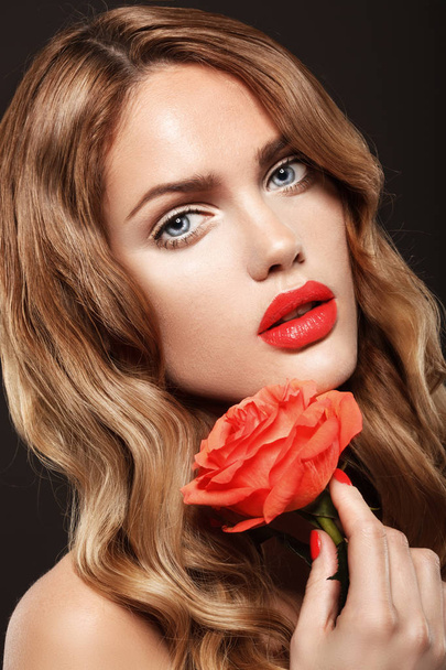 close up portrait of beautiful female model with red lips and wavy hair holding red rose - Фото, изображение