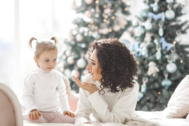 Joven madre y su hija se divierten cerca del árbol de Navidad en el interior
 - Foto, imagen
