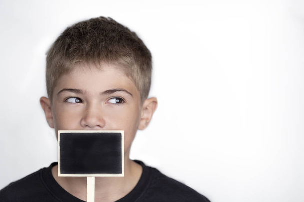 the youth's face close up,the teenager holds a black wooden sign at the mouth - Photo, Image