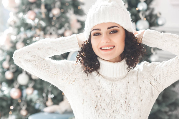 Young beautiful girl near the christmas tree smiling at camera. Cheerful pretty woman - Valokuva, kuva