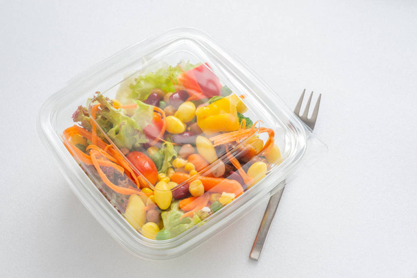 Mezclar ensalada en caja de plástico, tenedor sobre fondo blanco con luz natural
 - Foto, imagen