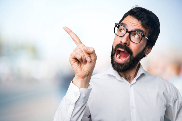 Handsome man with glasses pointing up on unfocused background - Photo, image