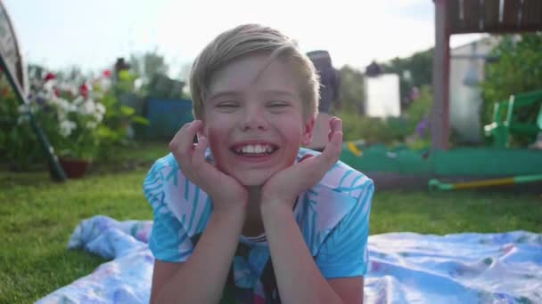 Der Kerl liegt an einem heißen Sommertag auf dem Rasen. das Kind ist lustig und aktiv in seiner Freizeit - Filmmaterial, Video