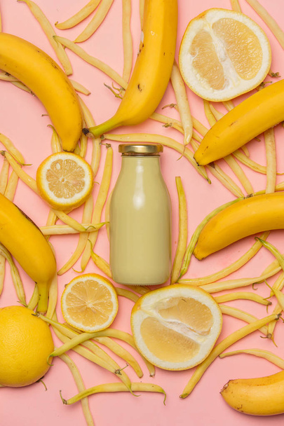 bottle of juce of lemons and bananas with peas on pink background. Above view - Photo, image