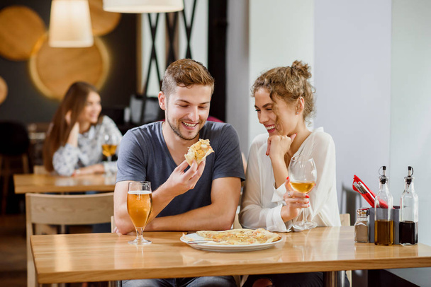 Sweet couple eating pizza and drinking beer and wine in pizzeria. - Foto, immagini