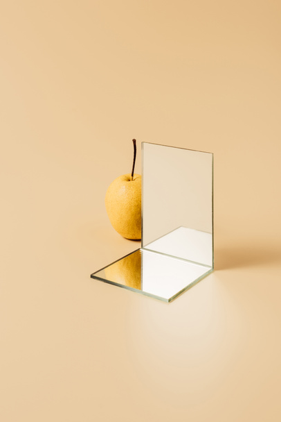 yellow pear and two mirrors on beige table - Photo, Image