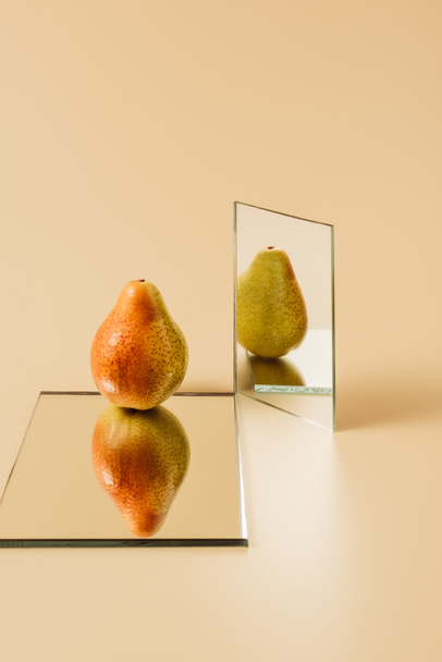 one ripe pear reflecting in two mirrors on beige table  - Fotoğraf, Görsel