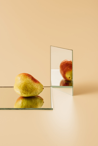 Gelbe Birne spiegelt sich in zwei Spiegeln auf beigem Tisch  - Foto, Bild