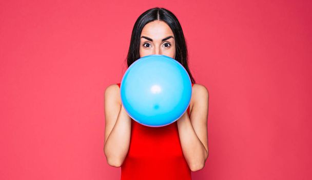 young brunette woman in red swimsuit posing with blue balloon on pink background  - Fotoğraf, Görsel