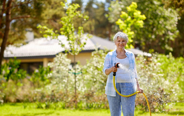 senior femme arrosage pelouse par tuyau au jardin
 - Photo, image
