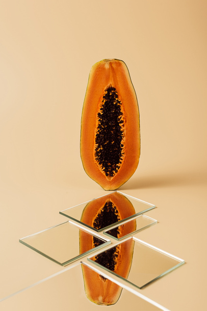 half of yellow papaya reflecting in mirrors on beige table  - Fotoğraf, Görsel