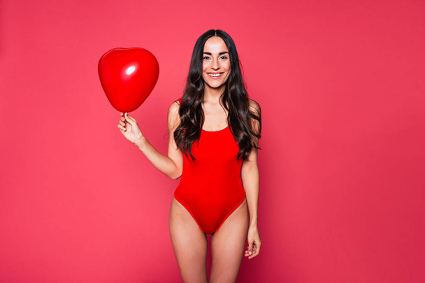 young brunette woman in red swimsuit posing with balloon on pink background  - Foto, Imagen