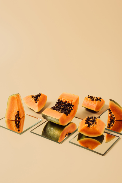 cut papayas reflecting in mirrors on beige table  - Photo, image