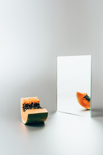 one piece of papaya reflecting in mirror on white table  - Zdjęcie, obraz