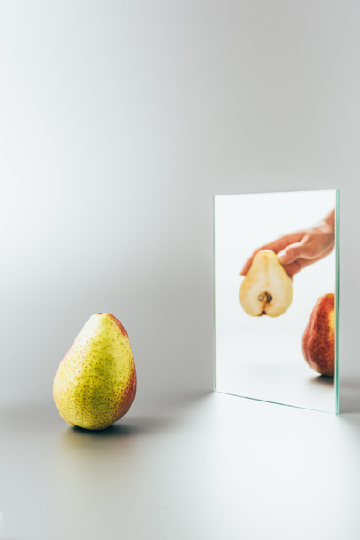 cropped image of woman holding yellow pear reflecting in mirror on white surface - Foto, afbeelding