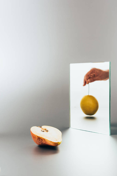 abgeschnittenes Bild einer Frau mit gelber Birne, die im Spiegel auf weißem Tisch reflektiert - Foto, Bild