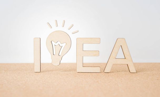 Business and design concept - wooden word " idea " and lightbulb on wooden desktop and white background - Foto, Imagen