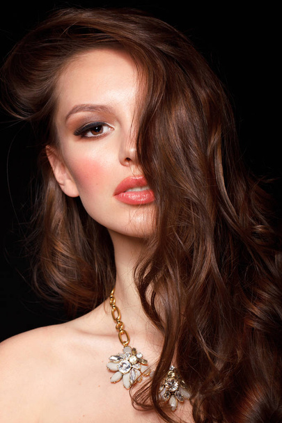 fashion portrait of sensual brunette woman with wavy hair and necklace on black studio background - Zdjęcie, obraz