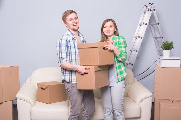 Семья, новая квартира, эмоции и концепция переезда - пара молодых счастливых людей складывают коробку вместе из-за переезда в новую квартиру и улыбаются
 - Фото, изображение