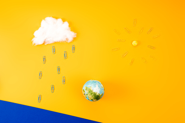 верхний вид композиции окружающей среды с земным шаром и облаком с солнцем из скрепки на желтом
 - Фото, изображение