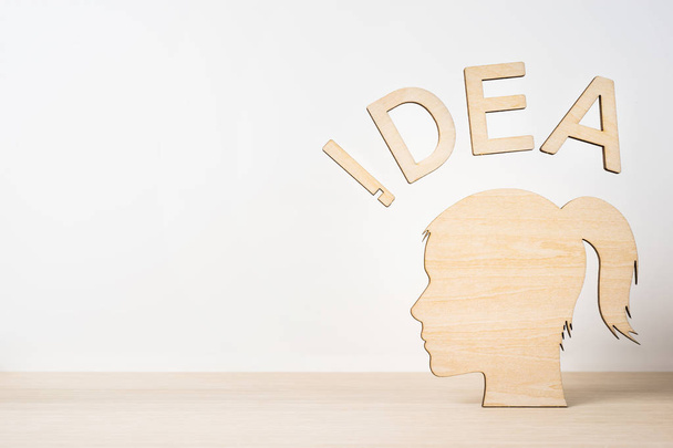 Concepto de negocio y diseño: cabeza de silueta de niña de madera con palabra "IDEA" en escritorio de madera y fondo blanco
 - Foto, Imagen