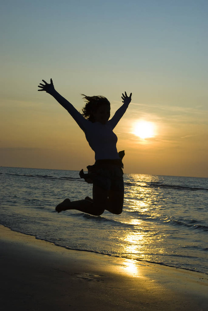 Женщина прыгает на берегу моря (на закате
) - Фото, изображение