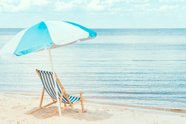 sun umbrella and beach chair on sandy shore near the sea - Foto, Imagem