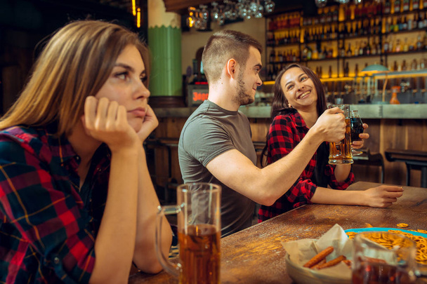 The people, leisure, friendship and communication concept - happy friends drinking beer, talking and clinking glasses at bar or pub and sad girl with negative emotions - Photo, image