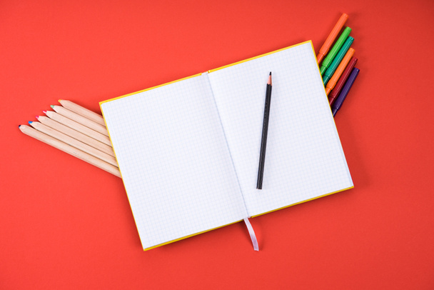 top view of opened blank notebook with color pencils and markers on red - Fotografie, Obrázek