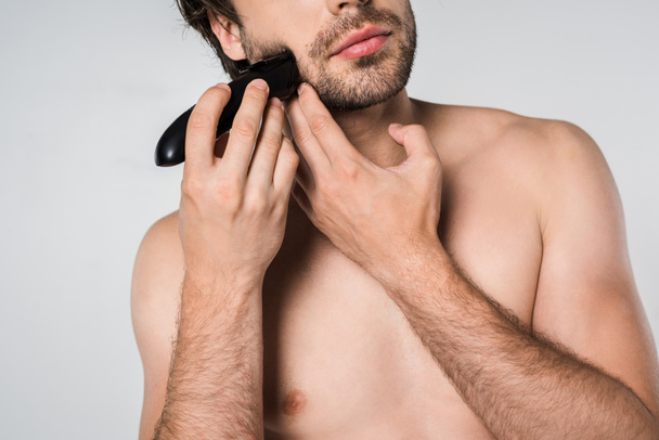 partial view of shirtless man with electric clipper shaving beard isolated on grey - Fotoğraf, Görsel